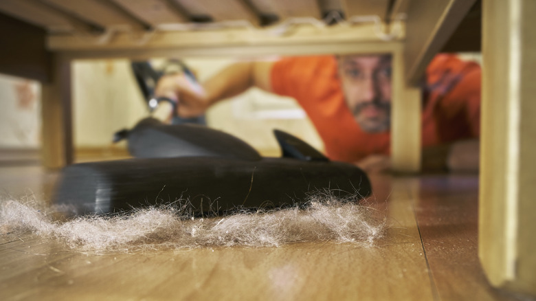 Man vacuuming up dust and hair underneath bed
