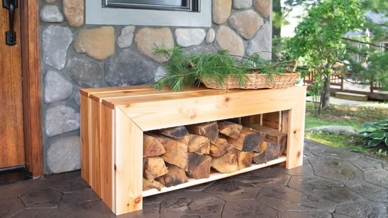 A wooden bench with firewood stored underneath rests outside the front door of a stone facade home.