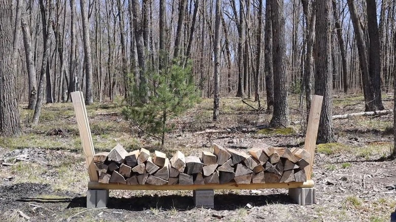 Firewood is stacked in a DIY rack made of cinder blocks and wood boards.