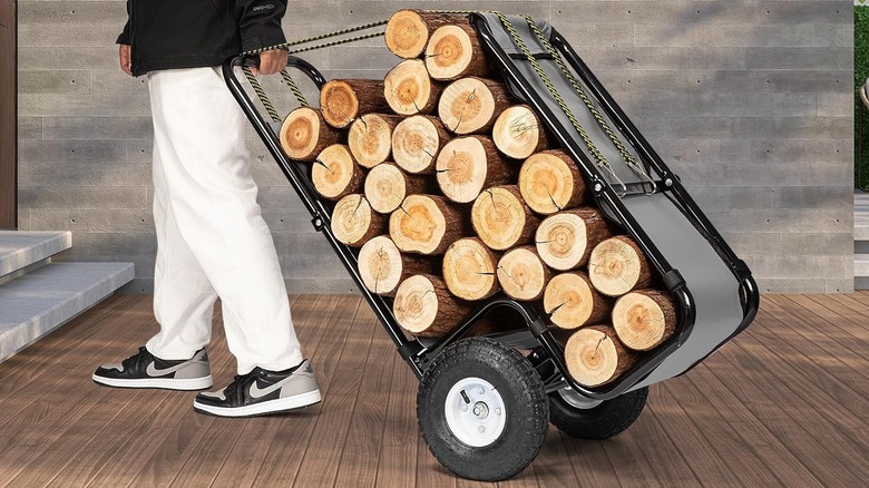 A man rolls firewood on a portable cart heading for stairs.
