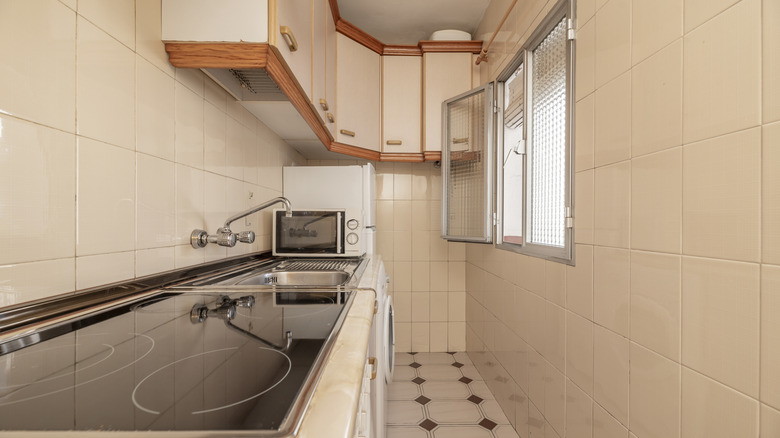 A kitchen with the counter, cabinets, and appliances running along one wall of the kitchen and a window on the other.