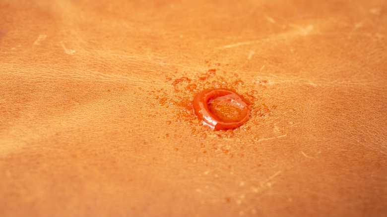A drop of fresh red candle wax on a tan leather couch.