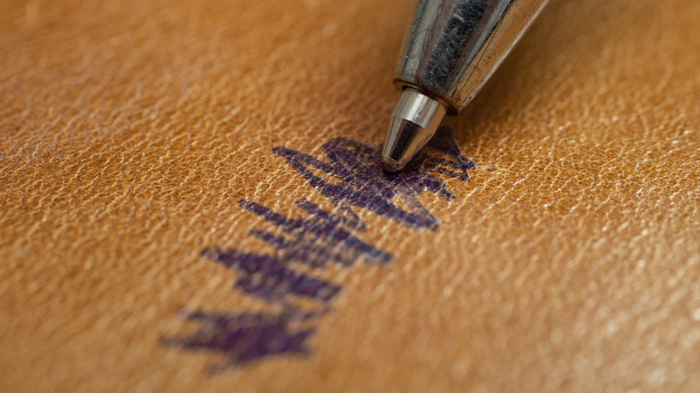 A pen nib scribbles with blue ink on the surface of a leather sofa.