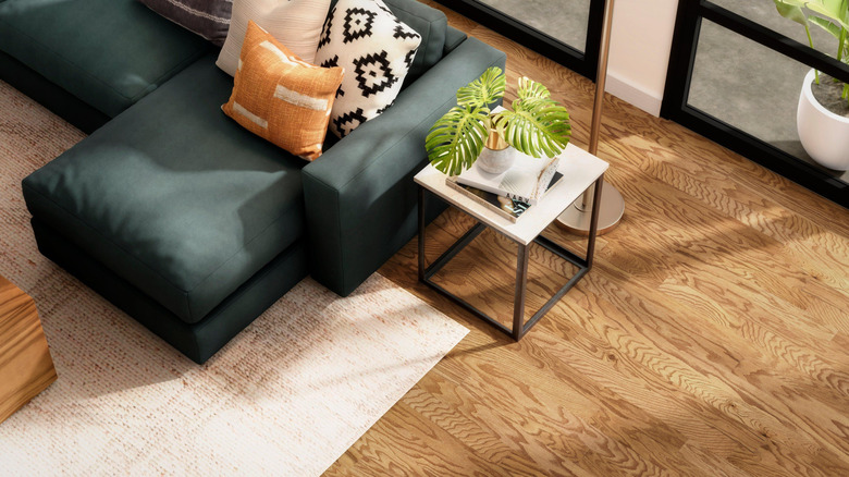 A caramel-colored hardwood floor with a rich green couch and a cream rug on top