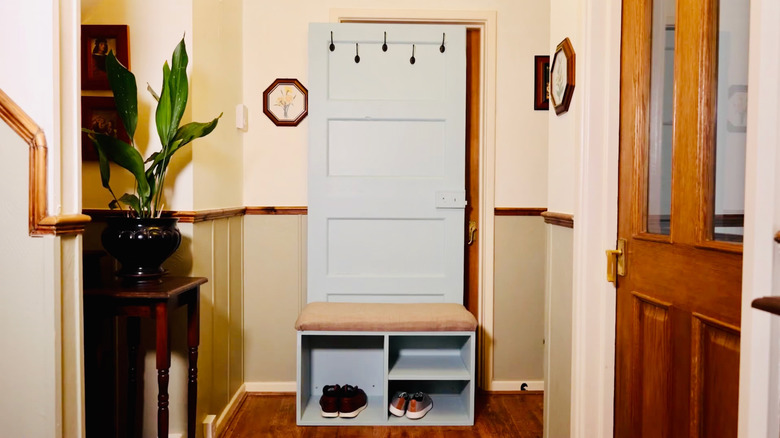 A hallway organizer made from an old door has hooks for hanging coats and hats, an upholstered bench seat, and a cubby with shelving for footwear and more.