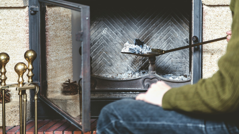 Person using a metal shovel to remove fireplace ash