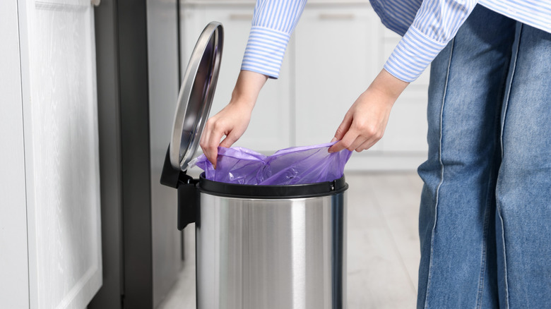 Person putting trash bag into garbage can in home