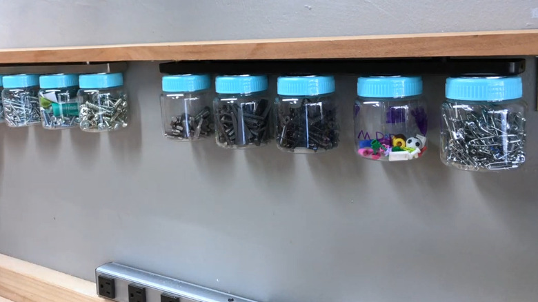 Jars holding nuts, screws, and other hardware along a magnetic knife rail mounted under a piece of wood