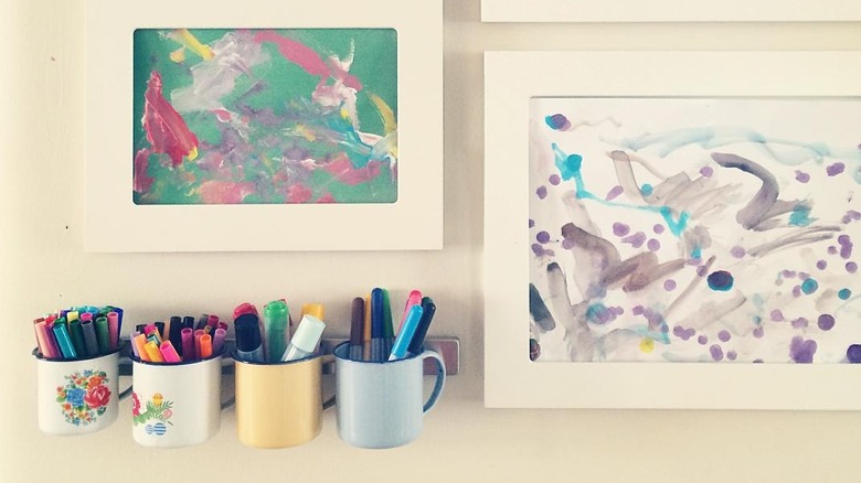 Magnetic knife rack holding steel cups of markers and pens next to some colorful artwork