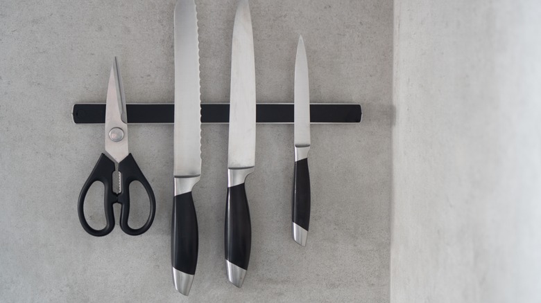 Three knives and a pair of scissors sticking to magnetic knife rack