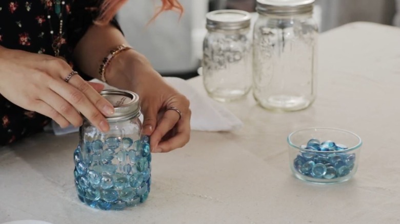 A woman glues glass gems to a jar.