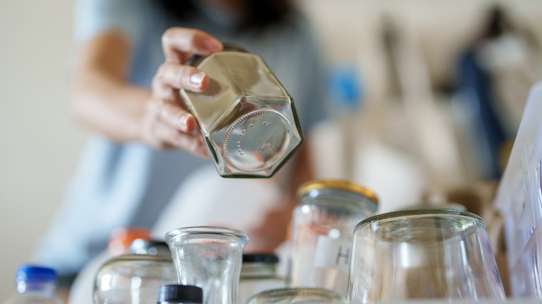 A person holding a glass jar above a collection of more glass jars.