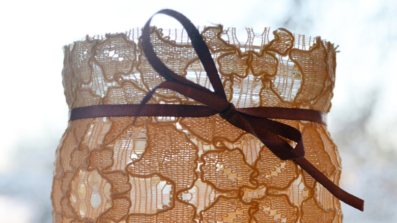 A glass jar covered with lace and tied with a ribbon.