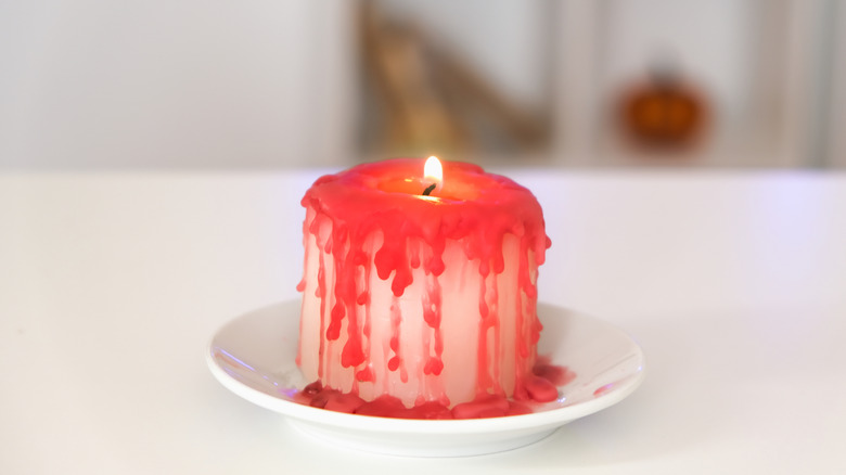 lit white candle on saucer with red wax running down it making it look like it's bleeding