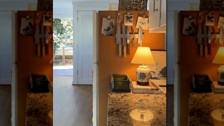 The side of a refrigerator lined with cork with knives and other items hanging on it