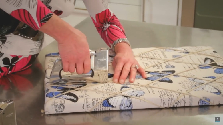 A person using a stapler on a cork board covered in fabric and cord
