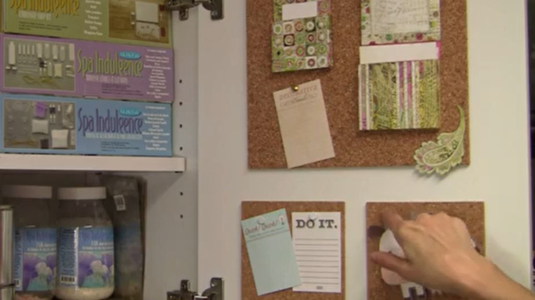 An open cabinet with a person sticking notes to a cork sheet installed behind the door
