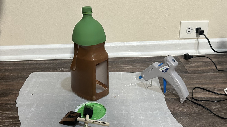 plastic bottle bird feeder with 2-liter bottle roof on a wood surface covered with parchment paper with paint sponges and a hot glue gun