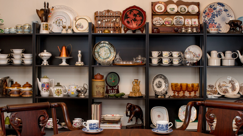 Vintage dishes and other trinkets on a large shelf behind a dining table and chairs.