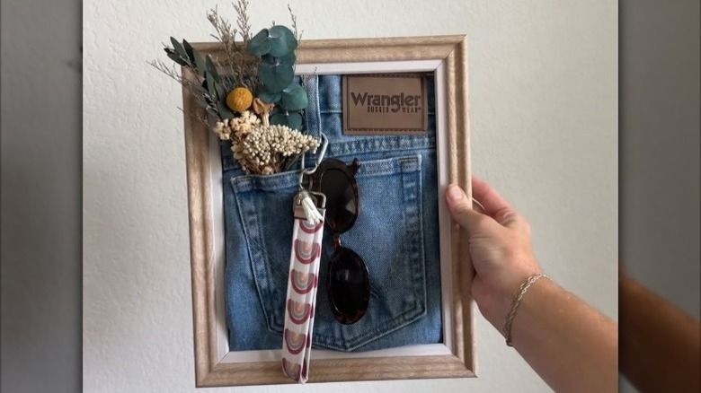 A framed jean pocket being used as storage for key lanyard and sunglasses