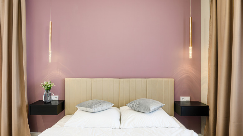 A bedroom with a mauve accent wall, hanging lights, and tan curtains.
