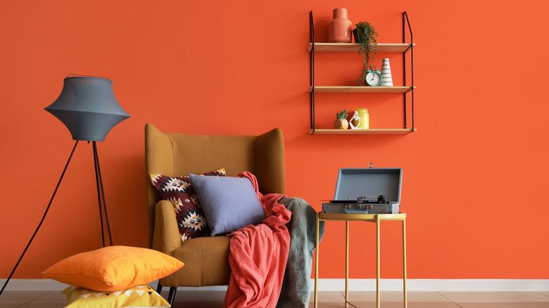 Red orange wall in a living room with a chair, lamp, and floating shelves