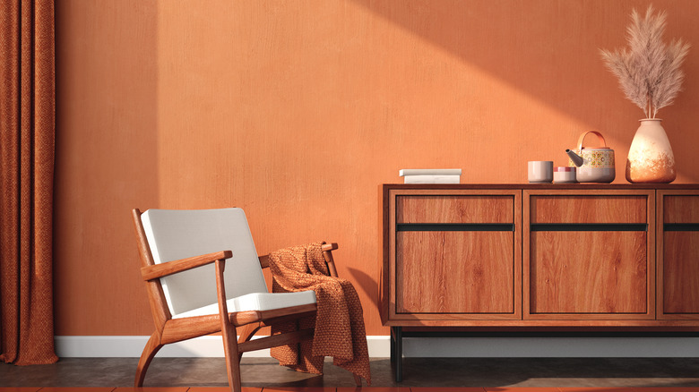 Burnt orange wall with an armchair and wooden dresser in the foreground