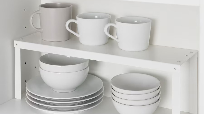 All white dishes and cofee mugs on white shelf insert in cabinetr