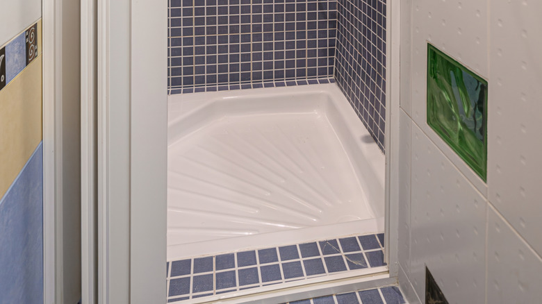 A diamond-shaped corner drain acrylic shower pan with textured lines leading to the drain