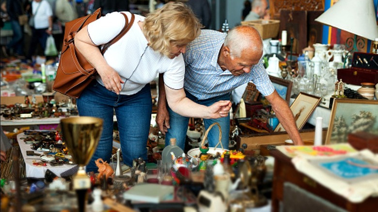 Two people are seen looking at a secondhand item at a flea market