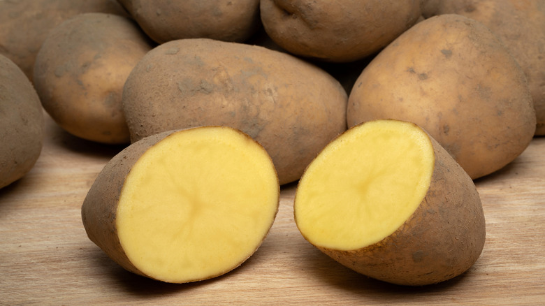 A bintje potato cut in half on a cutting board in front of a pile of whole bintje potatoes
