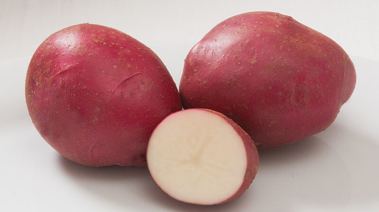 Two large, whole strawberry paw potatoes with a small strawberry paw half in front of them on a white backdrop