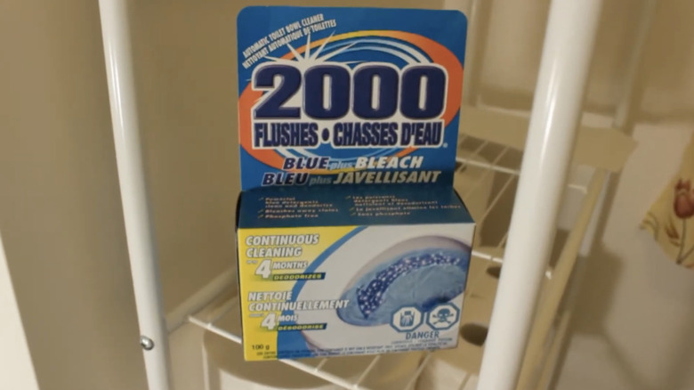A packet of 2000 Flushes sits on a wire shelf in a bathroom..