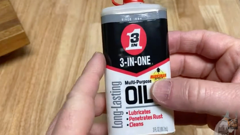 Two hands hold a bottle of 3-in-One above a wooden tabletop.