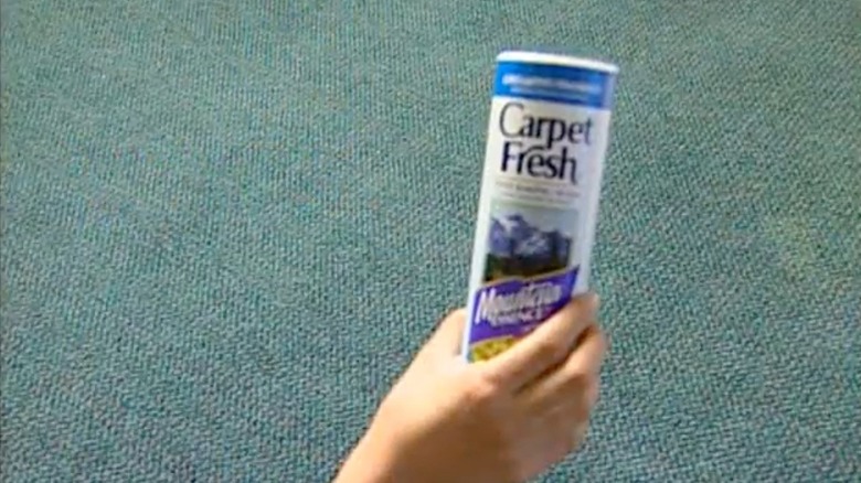 A can of Carpet Fresh held in a person's hand above a blue carpet.