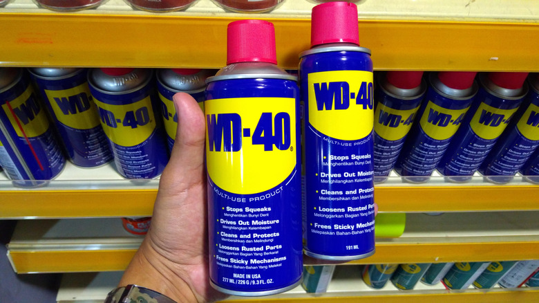 Two cans of WD-40 in a person's hand.