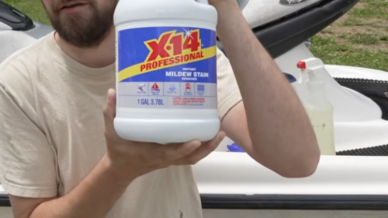 A man holds a bottle of X-14 while standing in front of a jet ski.