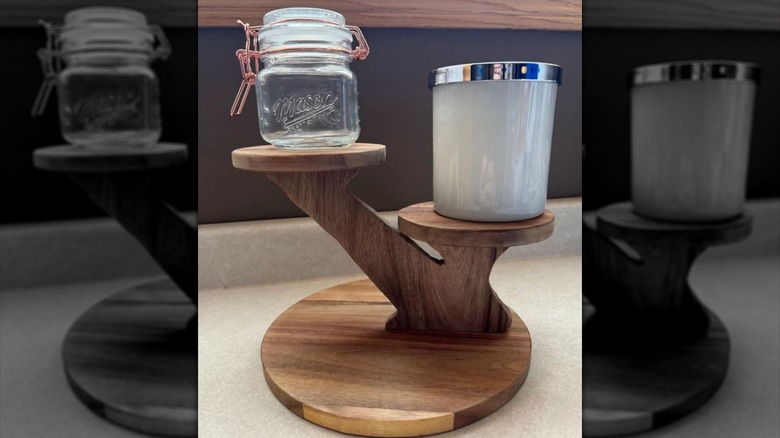 A wooden two-tiered plant stand holding a small jar and a candle.