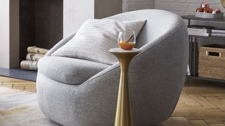 A small pedestal plant stand holds a single drink by a modern chair