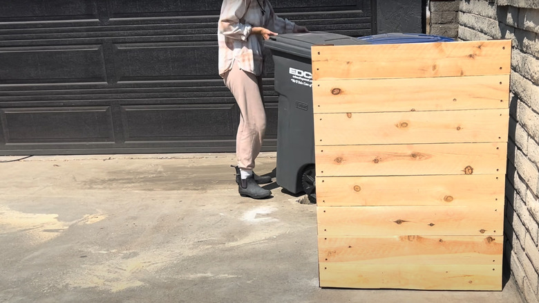 Woman hiding outdoor garbage bins behind DIY fence screen