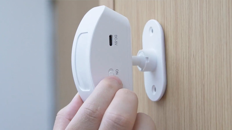 A hand places a motion detector on a wall