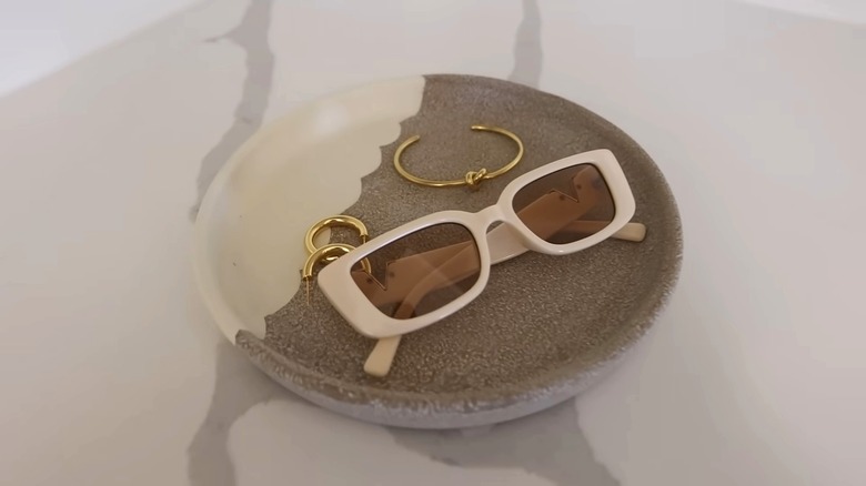 A painted plant saucer holding sunglasses and jewelry