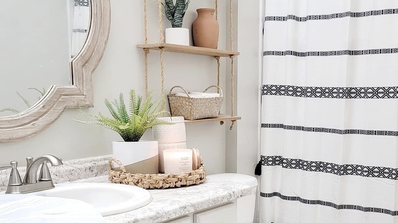 A candles, a plant, and other accessories in a basket on the vanity countertop in a bathroom.