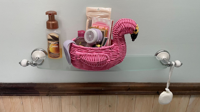 Makeup and beauty products in a small pink flamingo basket in the bathroom.