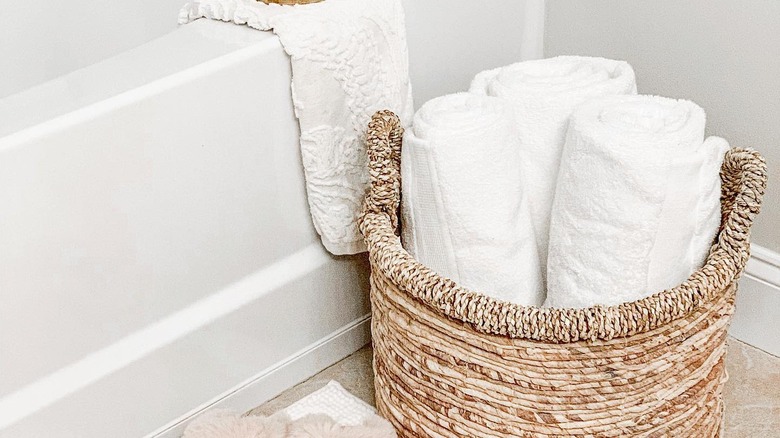 A basket of towels next to a tub in the bathroom.
