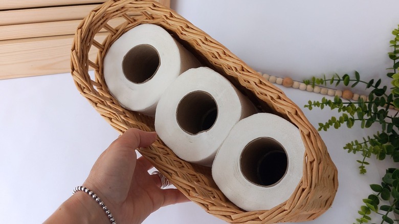 A hand holds a basket full of toilet paper rolls.