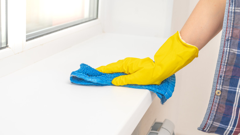 A gloved hand wiping the side table with a microfiber cloth.