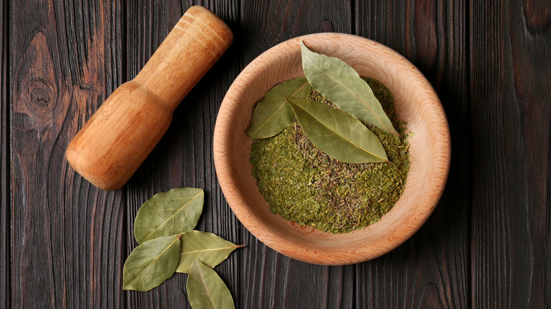 Mortar and pestle with whole and ground aromatic bay leaves on a wooden table.