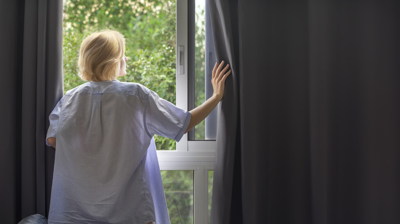 A woman closing dark blackout curtains.