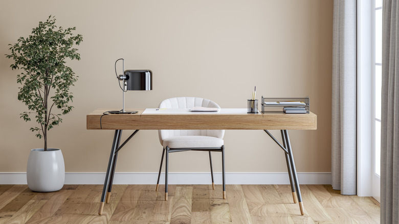 A simple office set up with blush-beige walls, a desk, and a modern lamp and chair.